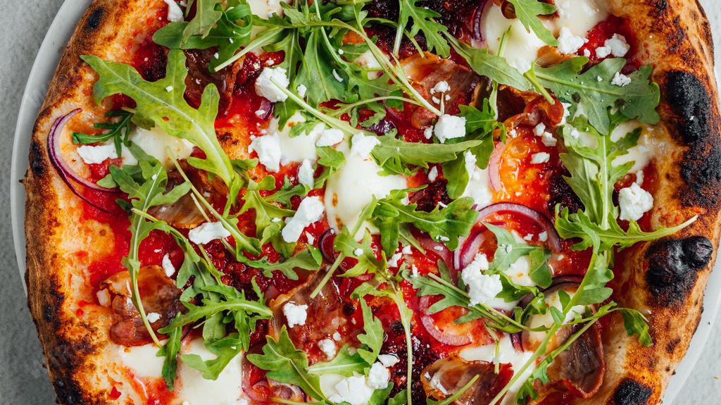 A delicious freshly baked homemade pizza with cheese, tomatoes and rucola on a white plate
