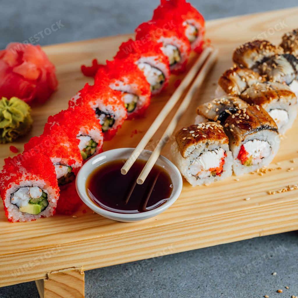 A wooden kitchen cutting board with an array of colorful sushi rolls displayed on top