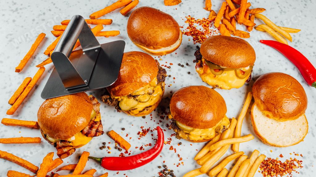 A closeup shot of tasty smash burgers, French fries, and red spicy pepper on the white background