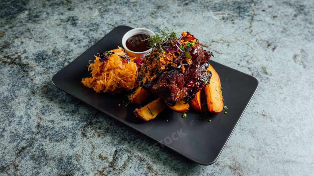 A closeup shot of beef meat with fried potatoes served in the black plate