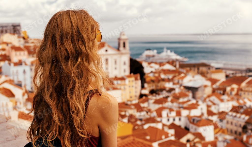 A young female tourist standing on a platform surrounded by fences and observing Lisbon at daytime in Portugal