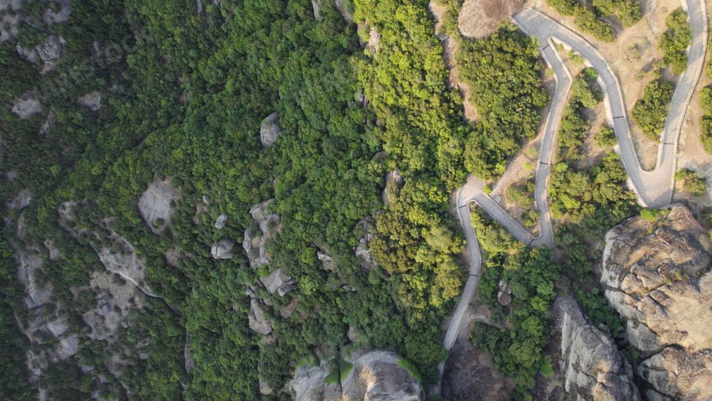 An aerial shot of the Meteora rock formation in Greece covered with vegetation and a curved highway