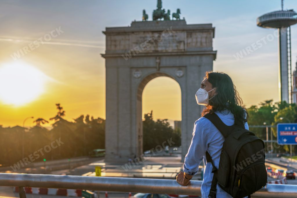 A young Hispanic male with a medical mask enjoying the beautiful view of a monument in Moncloa, Spain