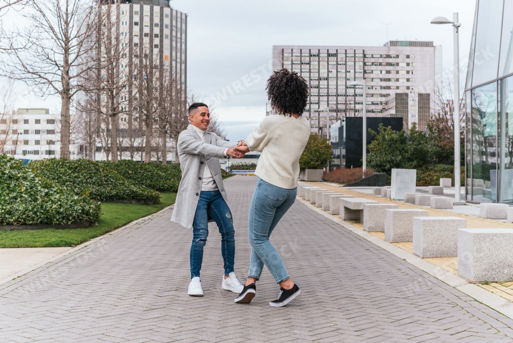 A shallow focus of a young cheerful couple spinning around near modern buildings