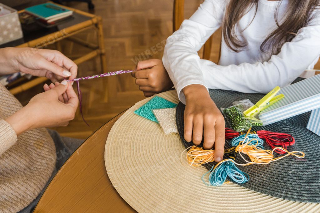 Hispanic cute girl making thread hand made bracelets at home