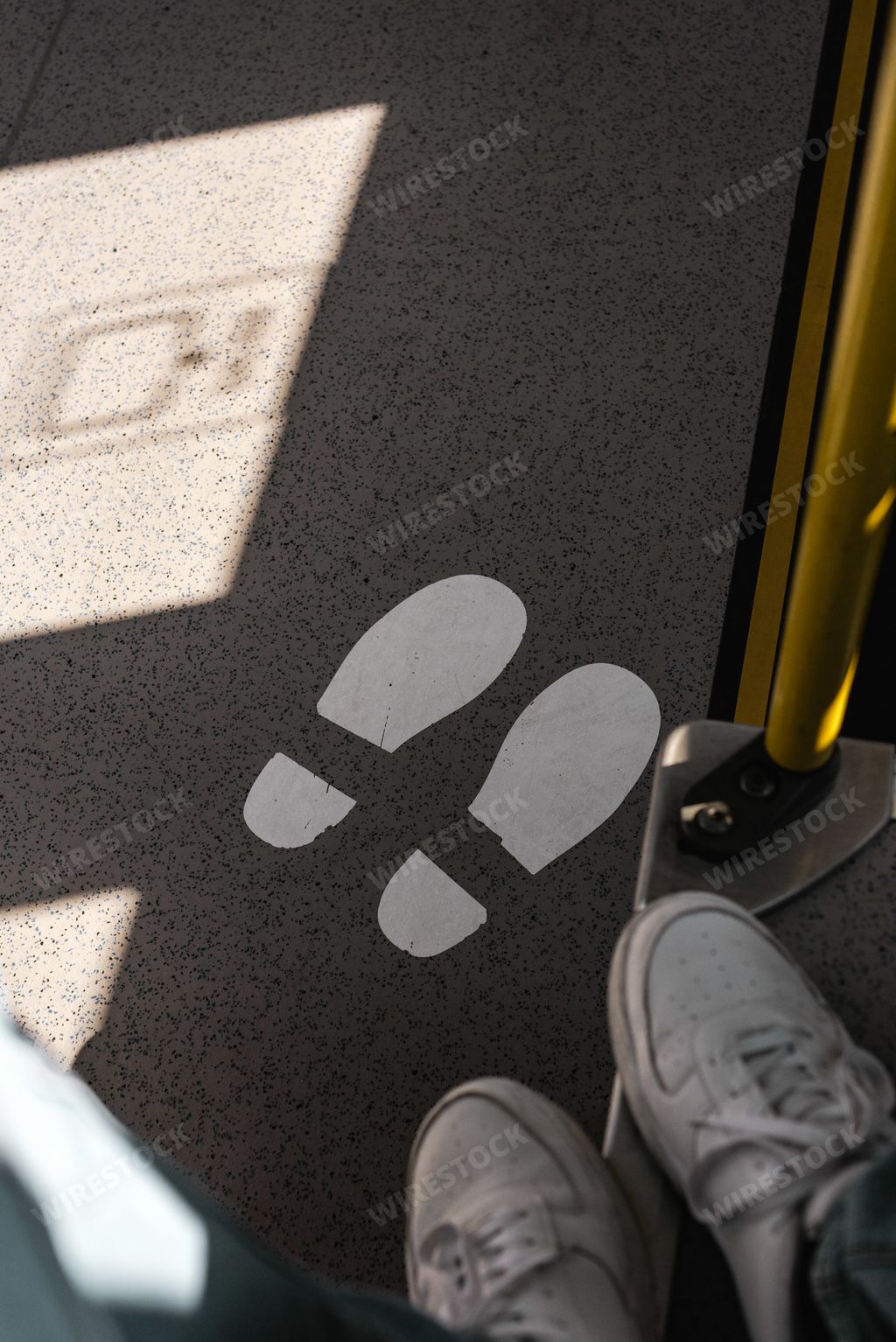 A vertical high angle shot of a person's feet near the feet sign for queue