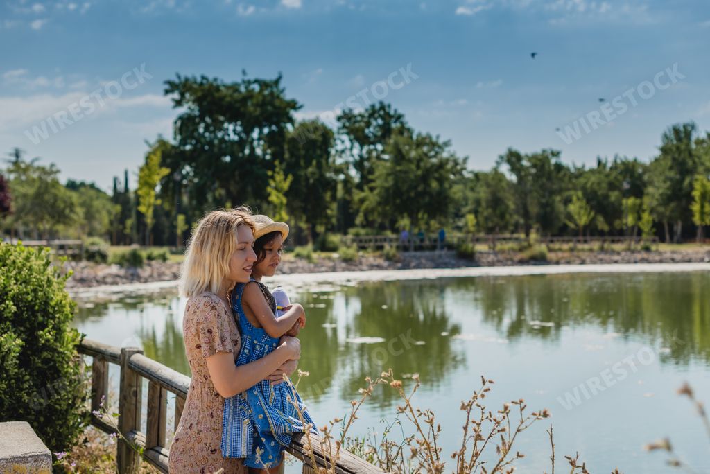 A blonde mom and her little daughter looking at the lake reflecting the trees