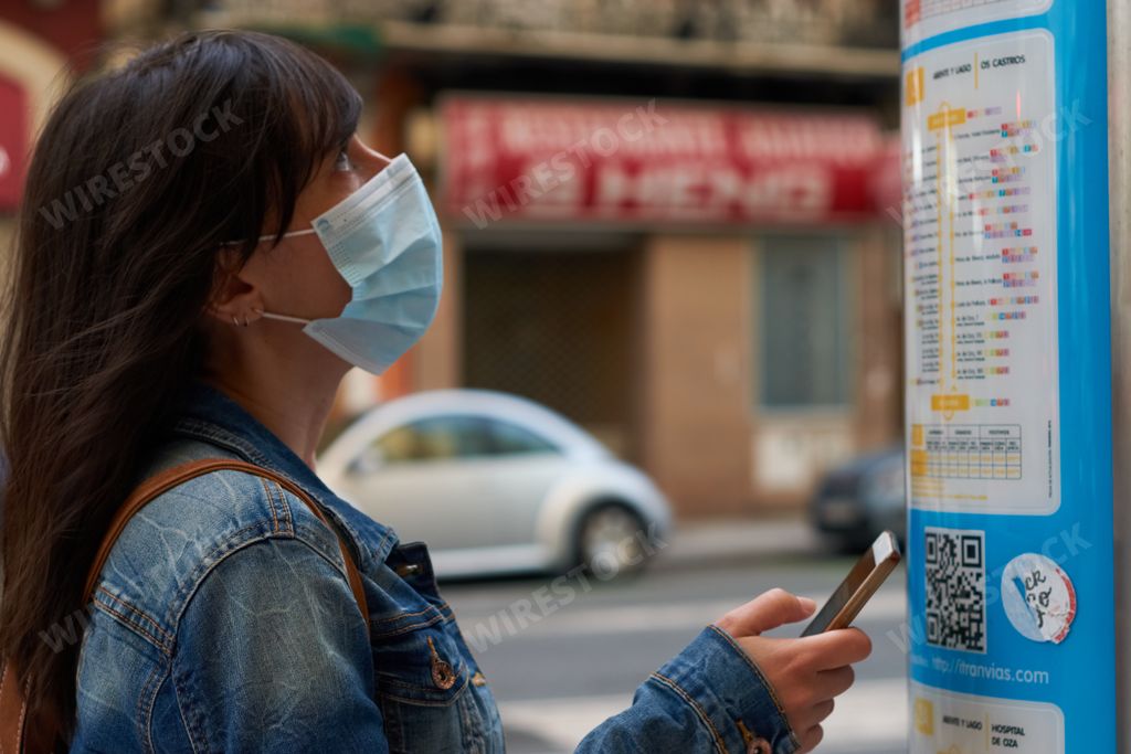 Girl with a phone in her hand checking the bus lines in the street.