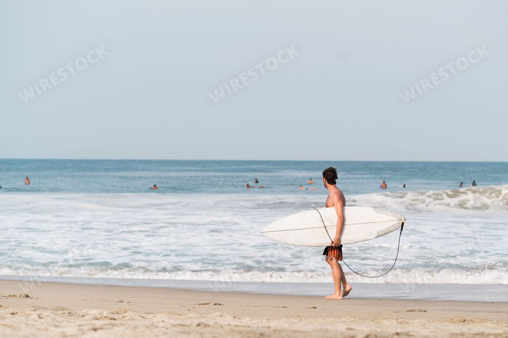 A surfer man holding surfboard and walking on the beach in Puerto Escondido, Mexico
