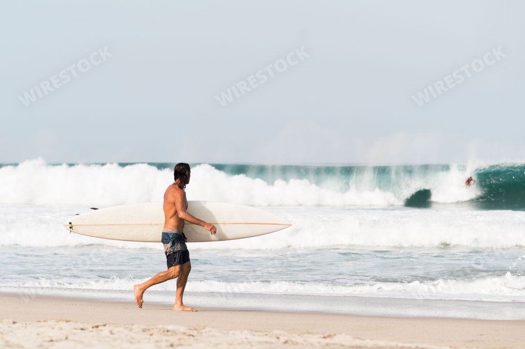 A surfer man holding surfboard and walking on the beach in Puerto Escondido, Mexico