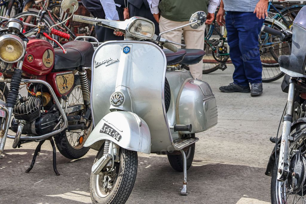 A classic silver metallic Vespa motorbike parked on display on a road