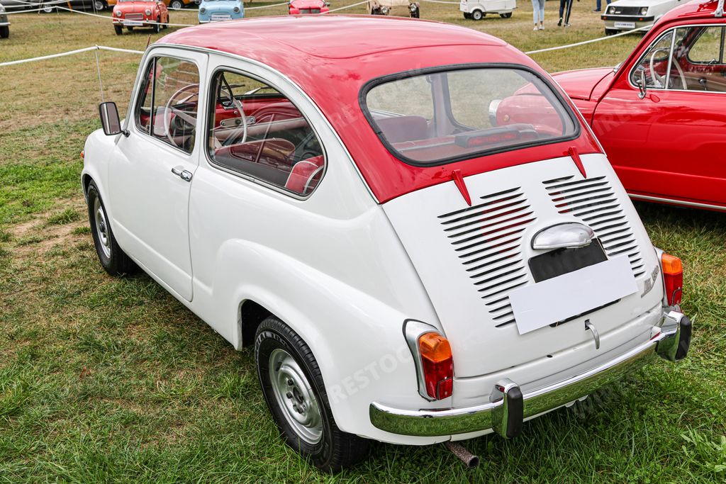 A rear view of a classic white Fiat model 600D small car with a red roof in a field