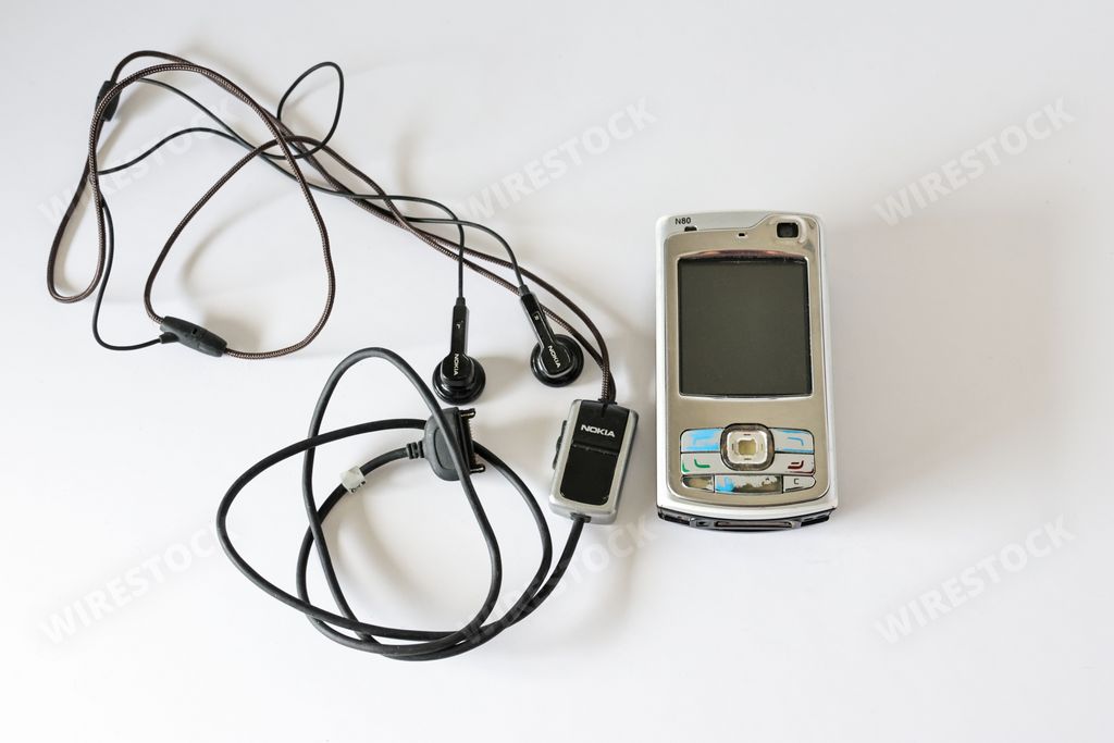 A vintage Nokia N70 GSMUMTS phone with wired headphones on a white surface
