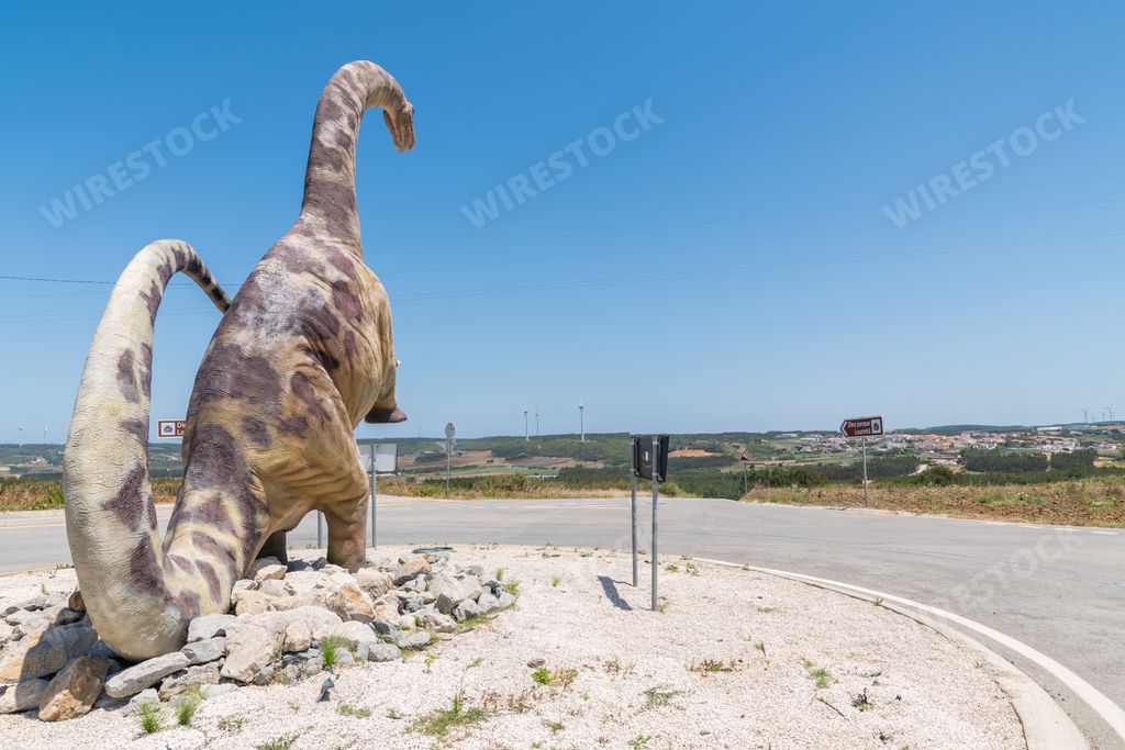 A roundabout road with a dinosaur model next to Dino Parque da Lourinha, Portugal on a sunny day