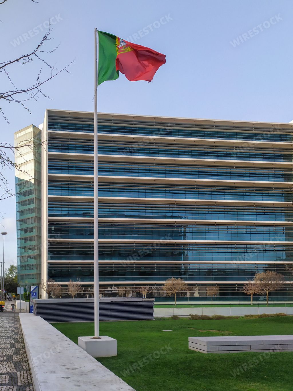 A vertical shot of the flag of Portugal waving in the air in the background of an office building.