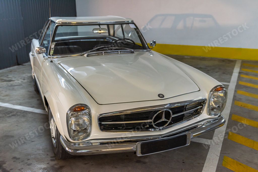 A closeup of the front view of a white vintage Mercedes-Benz model W113 car in a garage