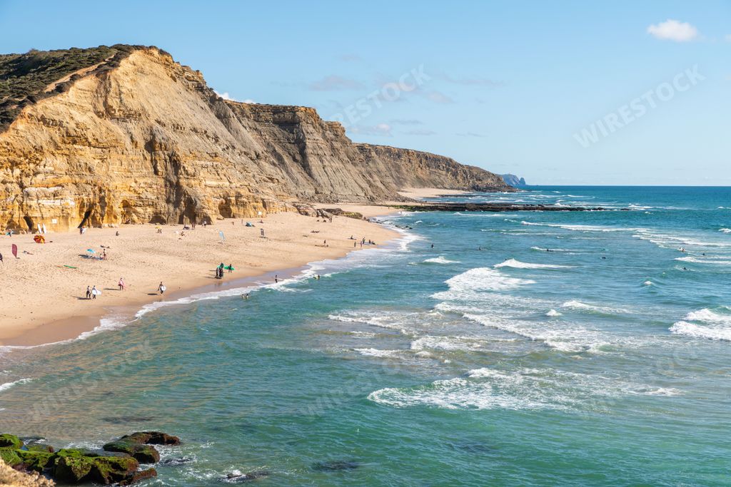 A scenic view of the Sao Juliao beach in Sintra,Portugal from a cliff with people sunbathing on the shore