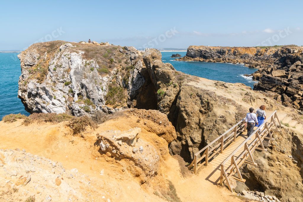 The people walking over a wooden bridge of the waterside cliffs under the blue sky in Ilheu da Papoa