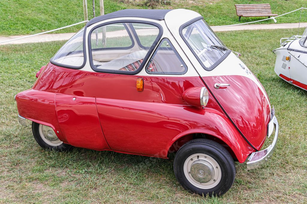 A side view of a beautiful classic three-wheel red BMW Isetta 300 in a field
