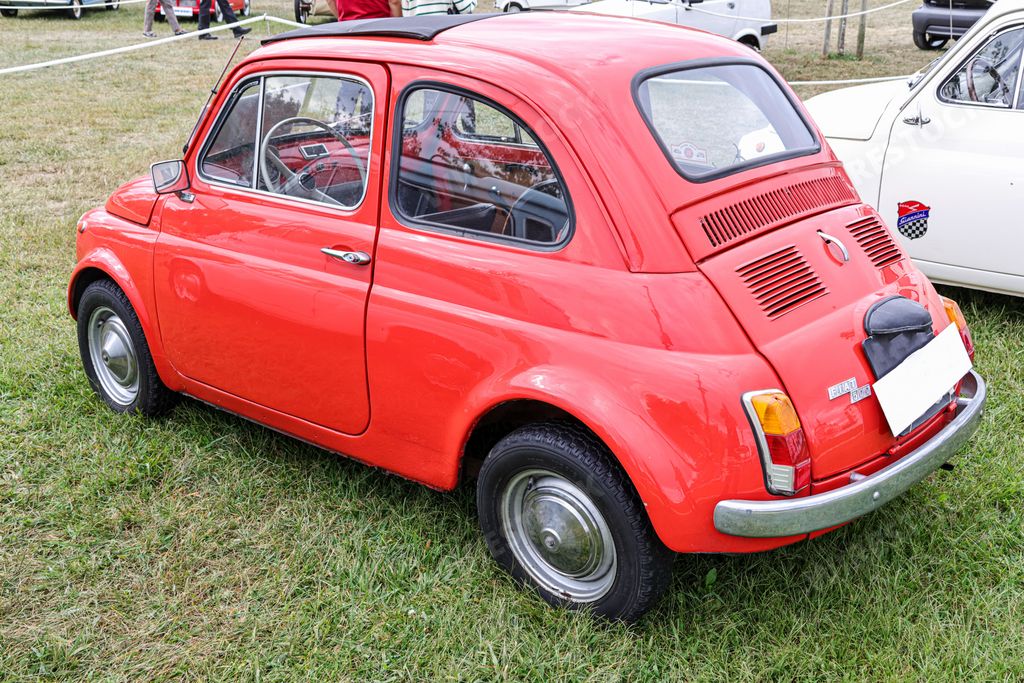 A rear view of a classic red Fiat model 600D small car in a field