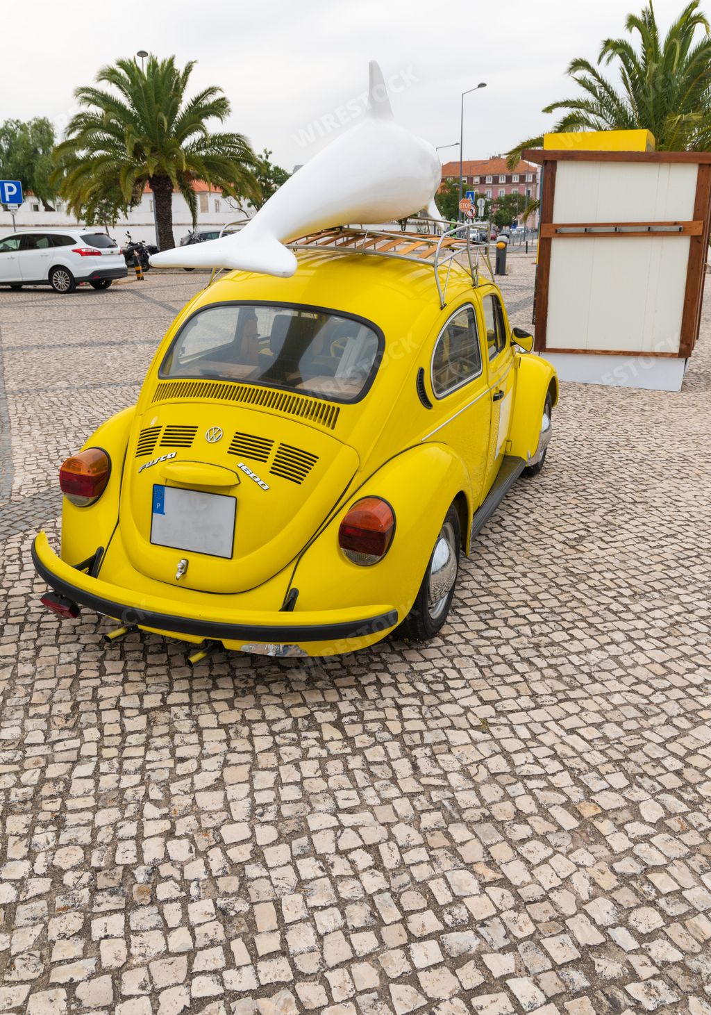 A vertical shot of a vintage yellow Volkswagen beetle car with a dolphin figure on a cobblestone road