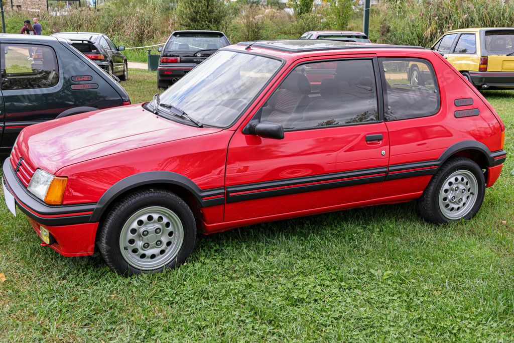 A classic red sports car Peugeot 205 GTi standing on the green grass