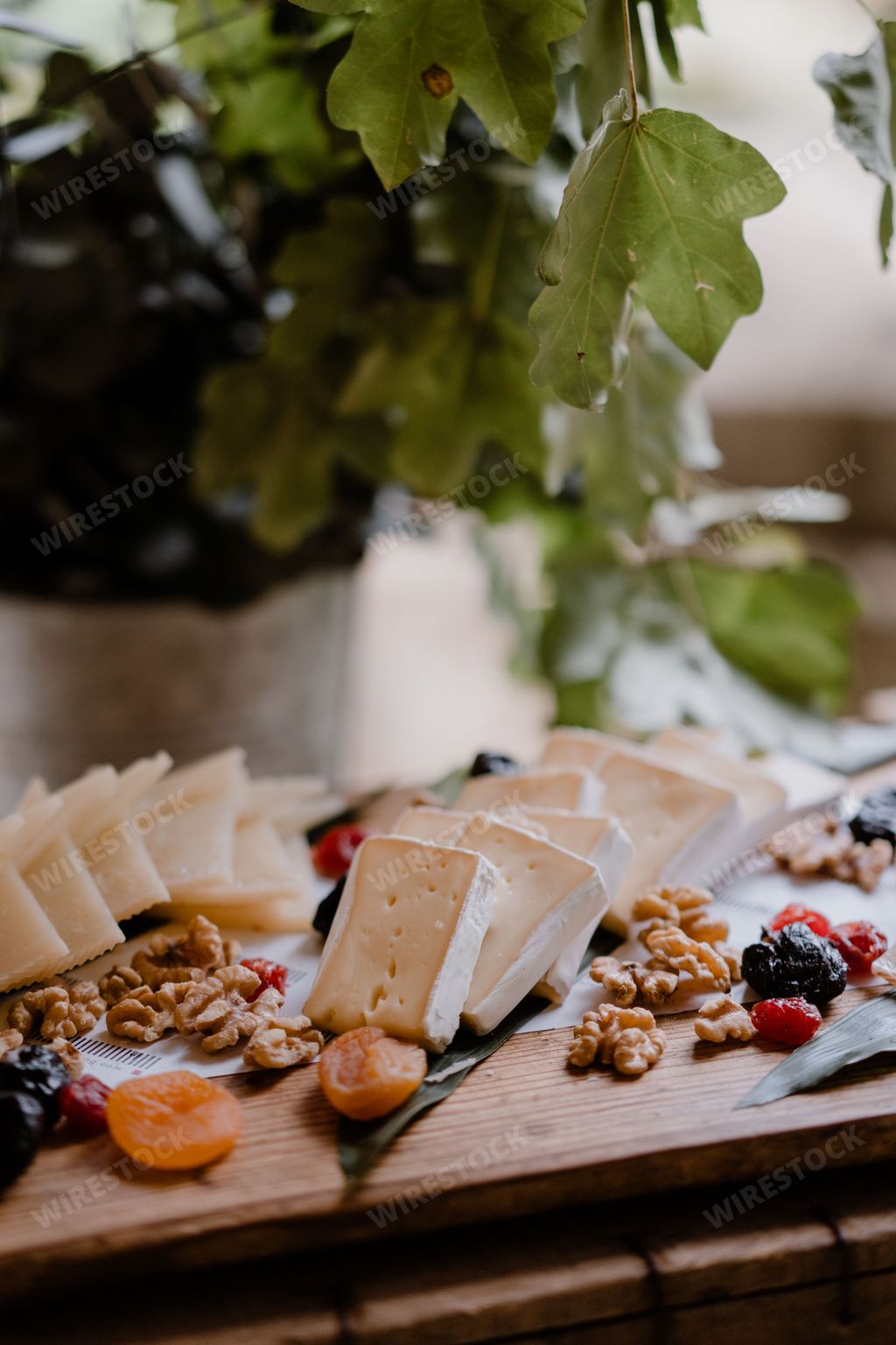 A vertical shot of cheese varieties served with nuts and dried fruits on a wooden board