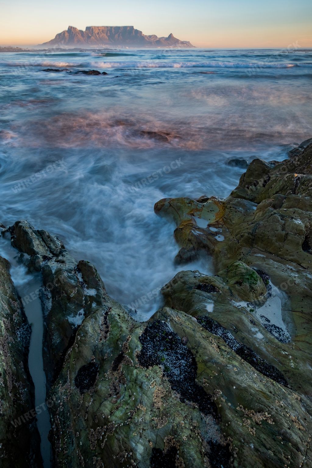 A vertical shot of ocean waves hitting the rocks on the shore