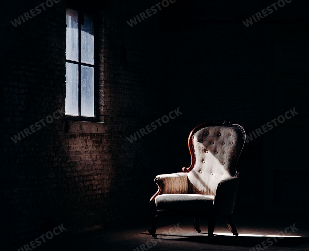 A beautiful shot of a retro chair in the dark empty room with a strip of window light falling on it