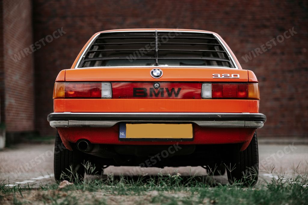 A close-up shot of the back of an orange classic retro BMW 320  car at a parking