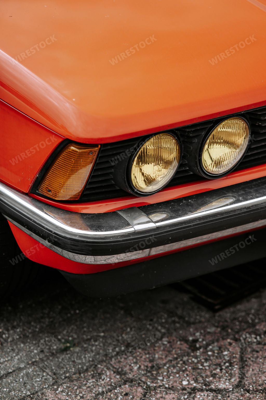 A vertical shot of the yellow headlights of an orange classic retro BMW 320  car