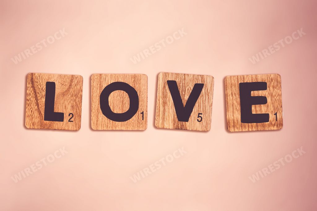 The word "love" written with wooden scrabble tiles on the pink surface