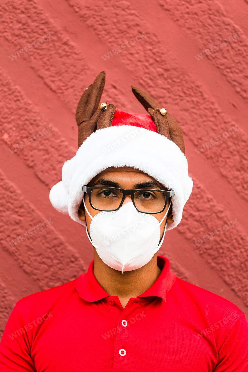 A vertical shot of a young man wearing a protective mask and a Christmas hat