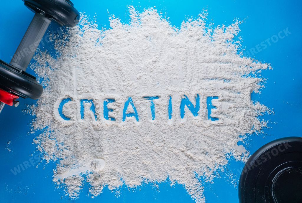 The word creatine written on a white scattered powder  on a blue background - concept of wellness