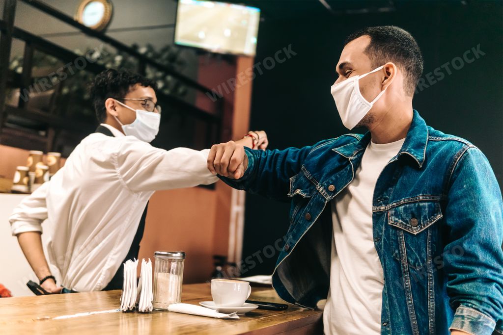 A customer and a bartender wearing face masks bumping their elbows in a cafeteria