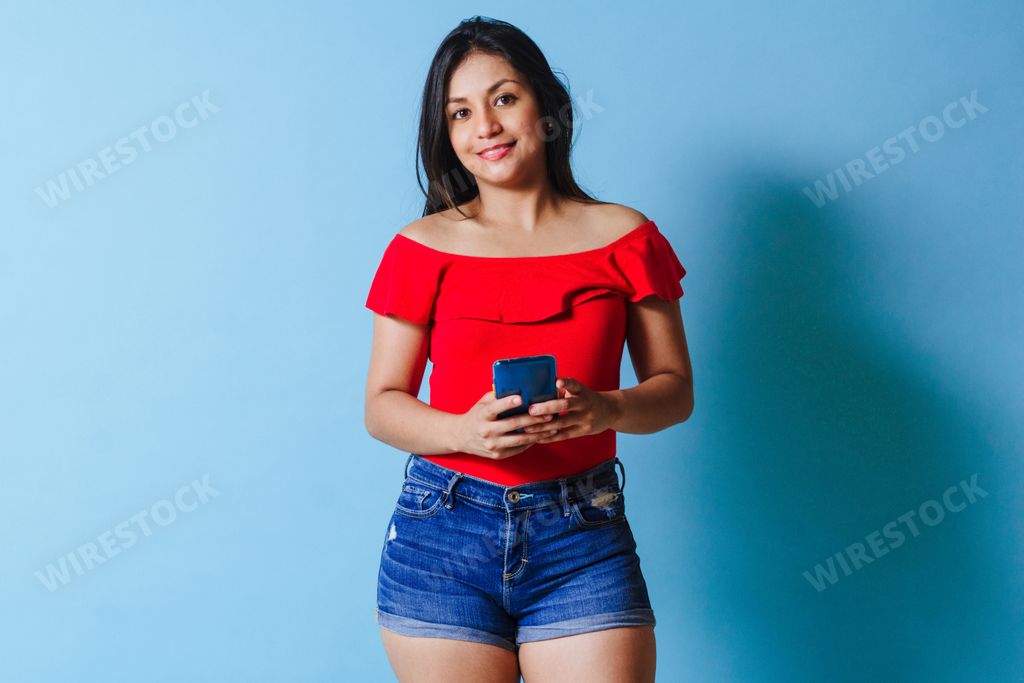 A young Latina using her smartphone on isolated blue background