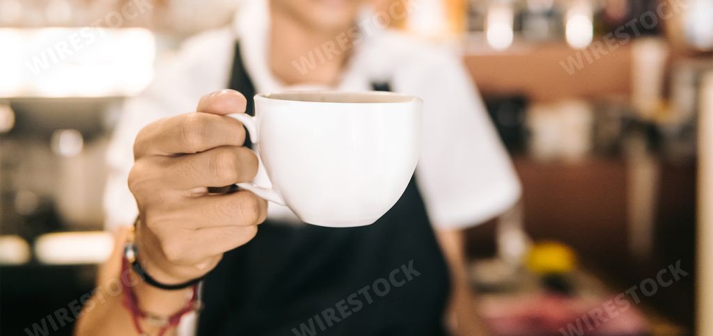 A closeup shot of a barista holding a cup of a delicious cappuccino