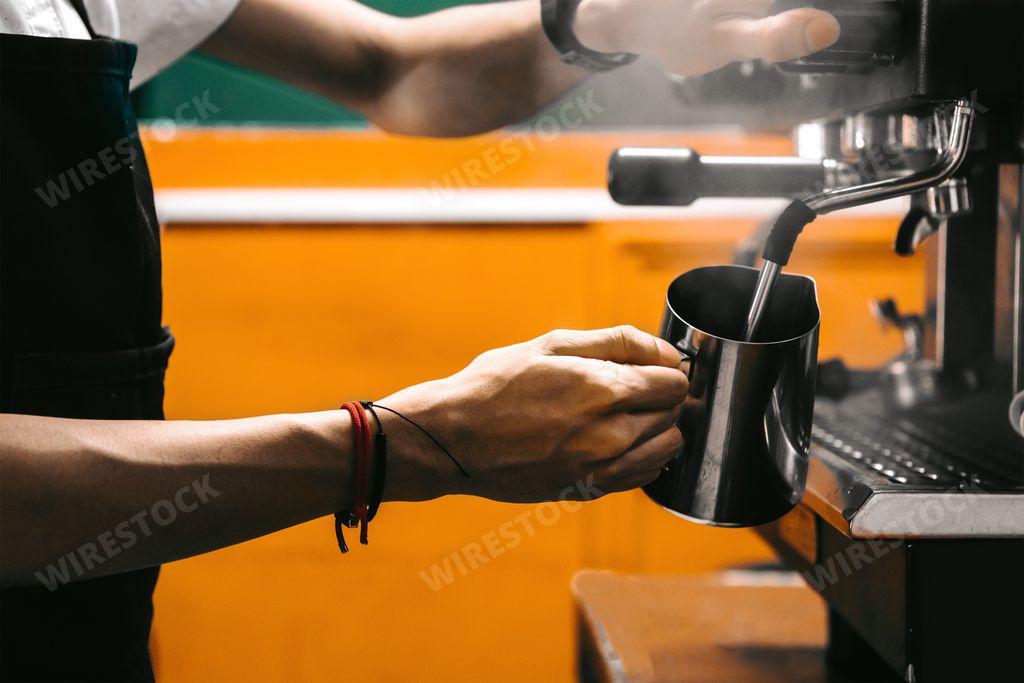A barista using a coffee machine filling it with milk - business and cafeteria concept