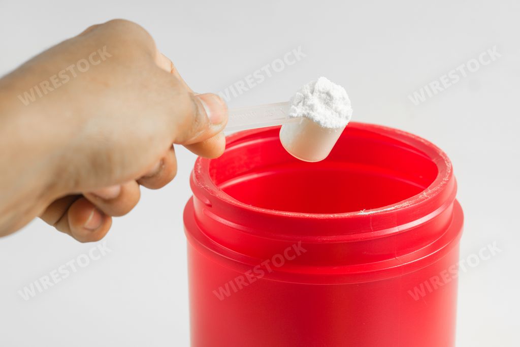 A hand holding a scoop of creatine over white background.