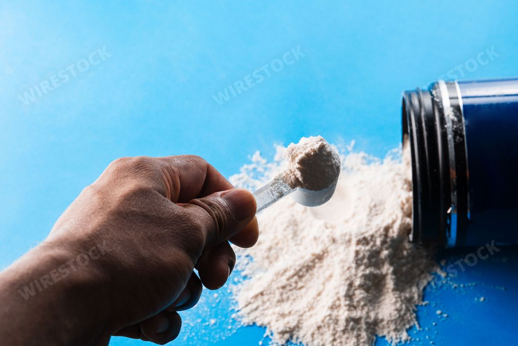 A male hand holding a scoop full of creatine powder on the background of scattered powder from the bottle