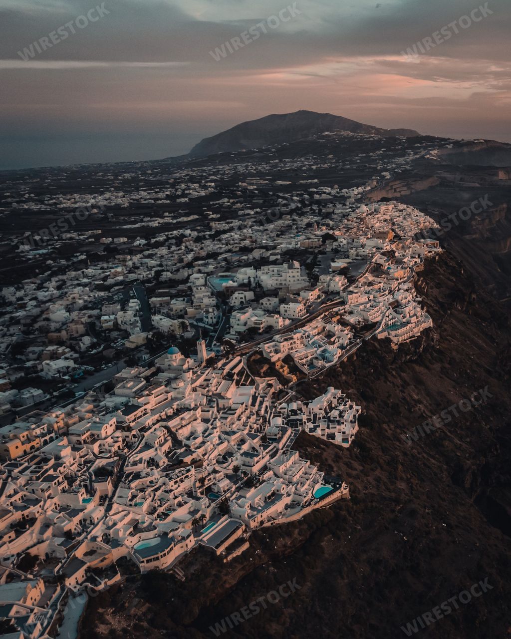 A beautiful vertical aerial view of the city of Thera in Santorini, Greece with blue and pink clouds in the sky at sunset