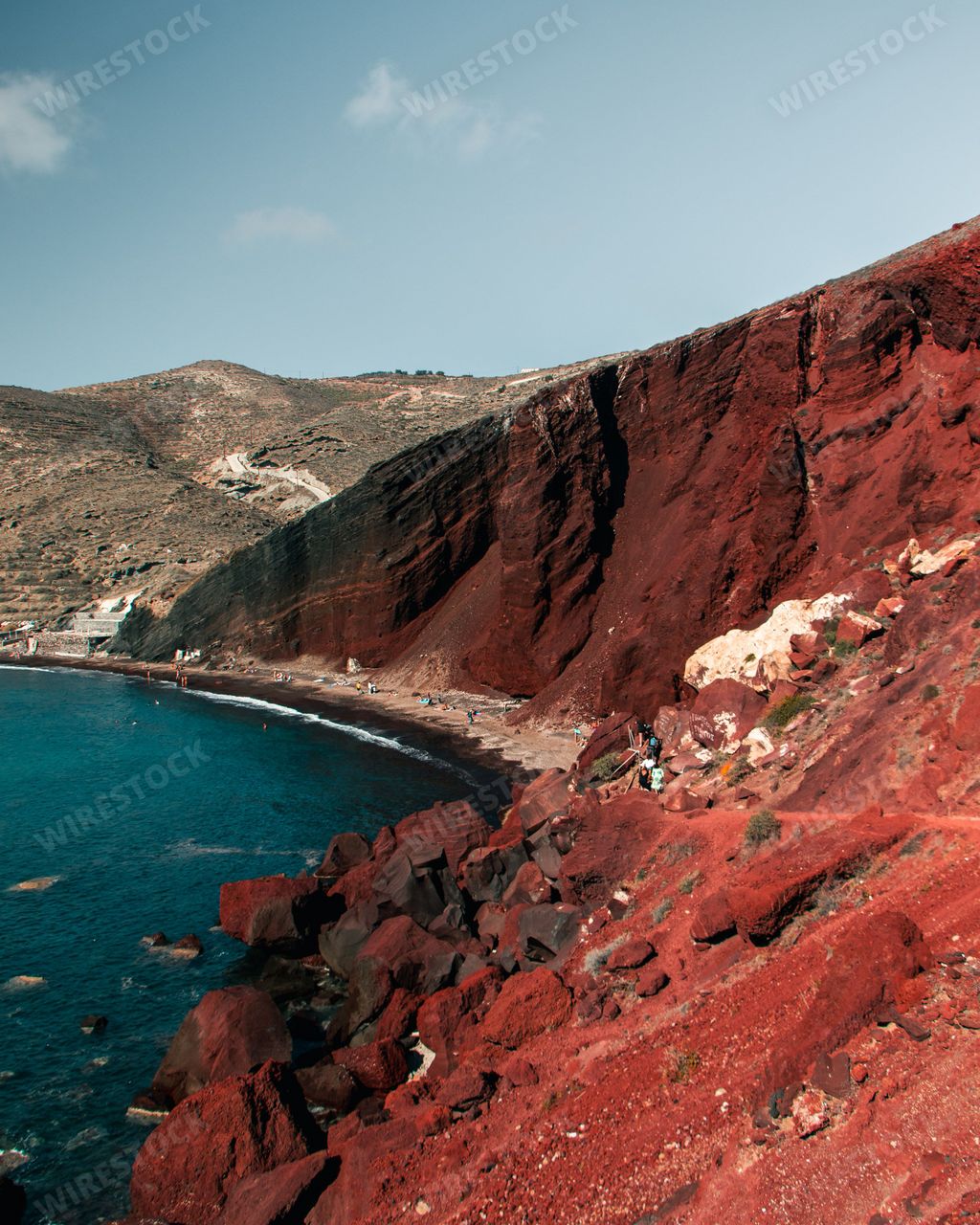 A gorgeous vertical shot of the Red Beach in Santorini, Greece with a dark blue sea under a pale sky