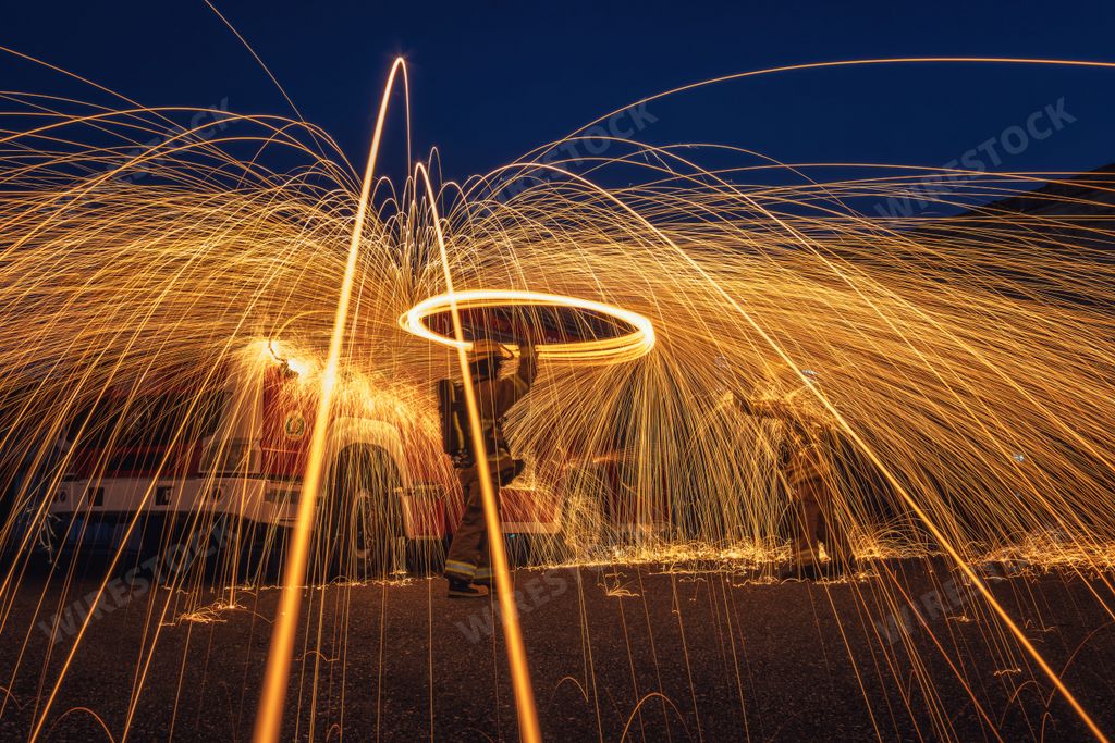 A high-angle shot of a spinning circle of steel wool illuminated by light trails, creating an abstract pattern on the ground