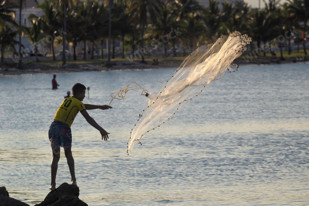 A young fisherman throwing a net in the bay
