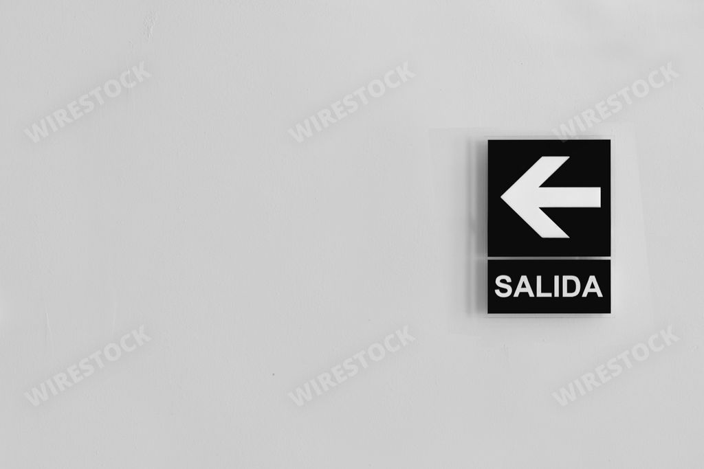 A grayscale exit (SALIDA) sign in Spanish with left arrow