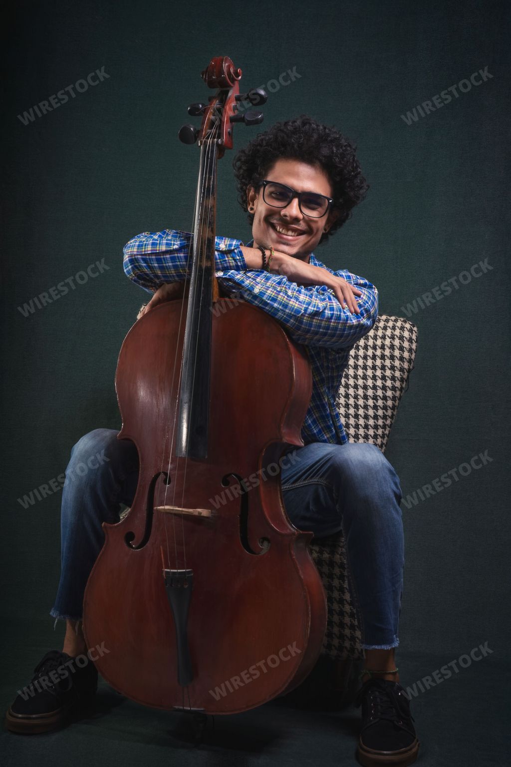 A vertical shot of a young male musician with a cello posing in front of a camera on a gray background