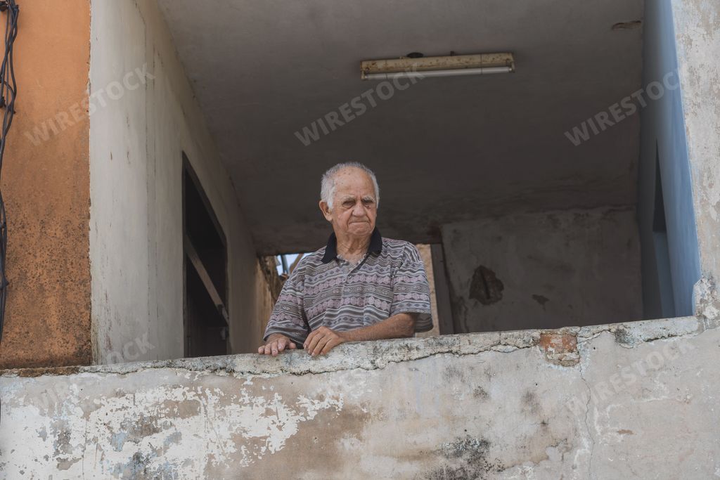 An elder man with sad face looking and leaning on the balcony of the old house in Matanzas, Cuba