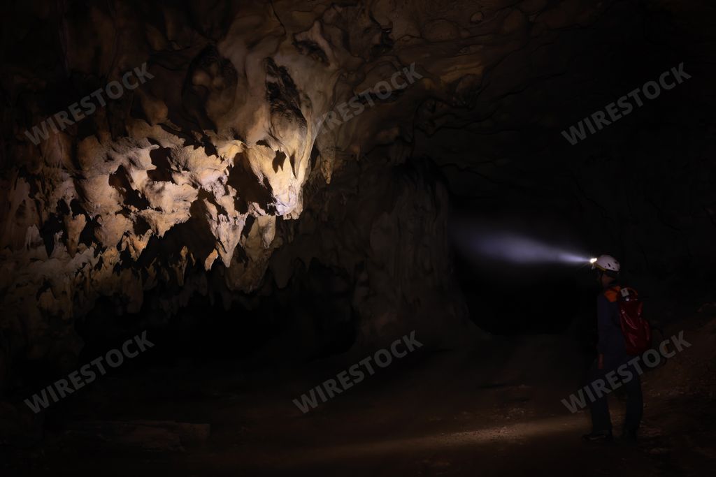 A male speleologist with helmet studying the walls of the dark cave