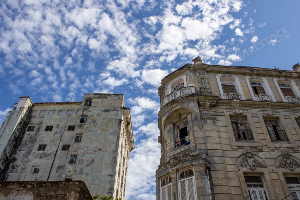 A view of buildings facade and windows in very bad condition in Habana, Cuba under the blue cloudy sky