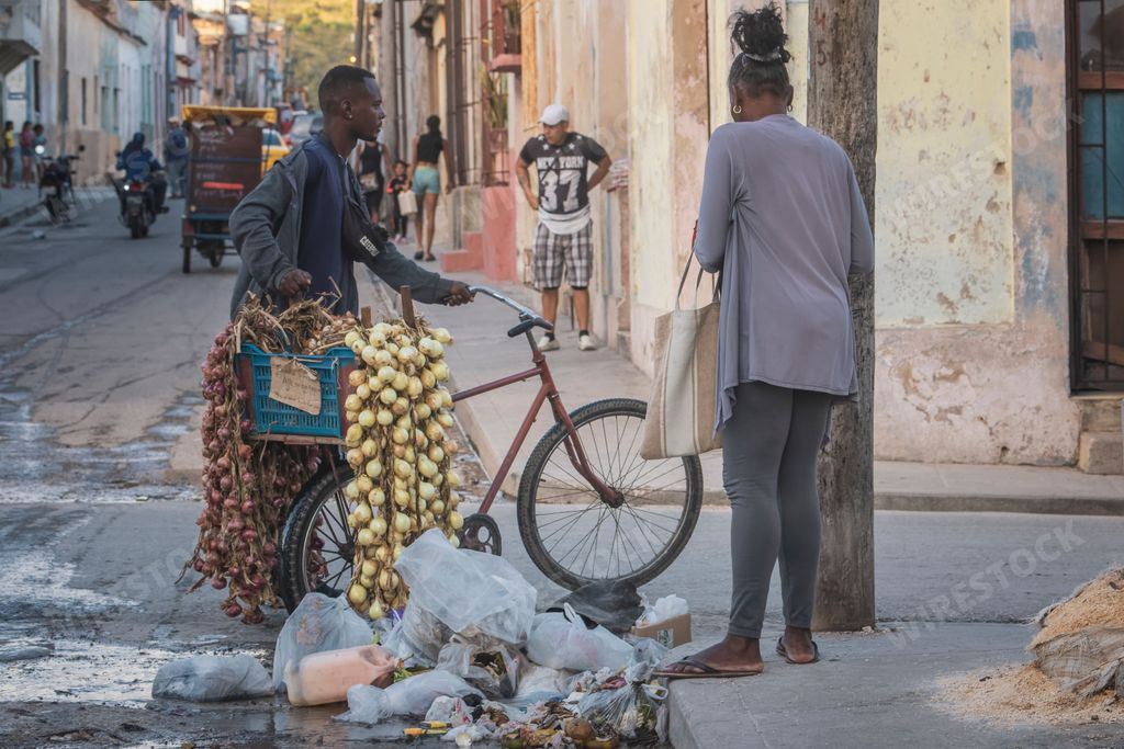 A Cuban street vendor is peddling his wares, transporting a basket of fresh onions on a bicycle